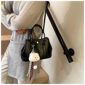 Detail of black glossy handbag with white cloud charm worn by model on stairs