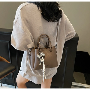 Detail of coffee brown lychee leather bucket bag with silver bow and woven rope charm