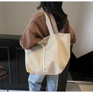 Detail view of large canvas tote bag with wide strap and gold studs on female model