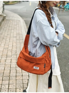 Outdoor shot of an orange crossbody messenger bag featuring a wide black strap and front pocket