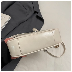 Primer plano de la base del bolso de cuero crema con costuras finas y hebilla plateada