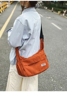 Outdoor shot of a bright orange crossbody messenger bag with side functional pockets