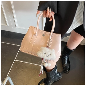 Detail of pink patent leather handbag featuring cloud plush charm and metallic clasp accent