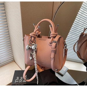 Close-up of pink bucket bag featuring lychee texture and metallic bow charm detail