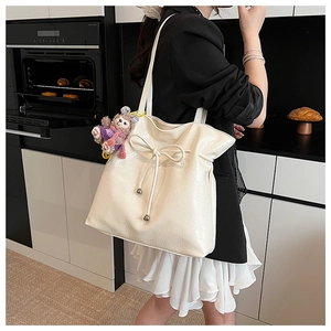 Détail d'un sac cabas crème avec nœud de serrage et breloque en peluche douce