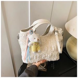 Détail d'un sac seau blanc plissé avec une breloque d'ours et des glands colorés