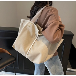 Detail view of beige canvas tote bag showing reinforced golden rivets and wide shoulder strap
