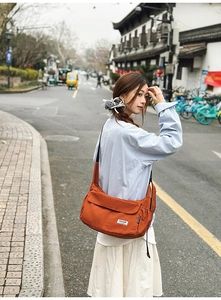 Detail of orange canvas messenger bag showing adjustable strap and side drawstring pocket
