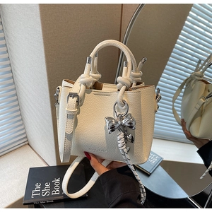 Detail of white lychee leather bucket bag featuring knot handle and bow charm