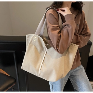 Detail of minimalist beige canvas tote bag with white trim and rivet accents on shoulder