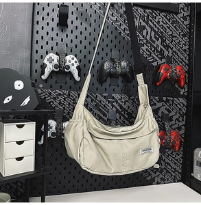 Detail of off-white nylon sling bag with brand tag and side pockets against a pegboard