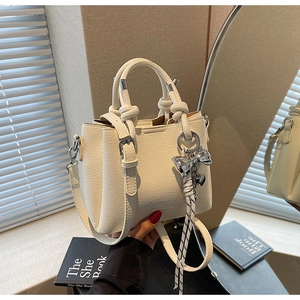 Close-up of white lychee texture bucket bag with knot handles and silver bow charm