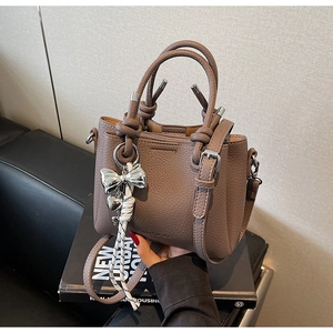 Macro detail of taupe lychee leather bucket bag with silver bow charm and knotted handle