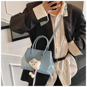 Close-up of light blue glossy leather handbag with cloud plush charm and shoulder strap