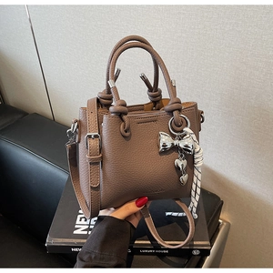 Close-up of brown litchi leather bucket bag featuring a silver butterfly heart charm