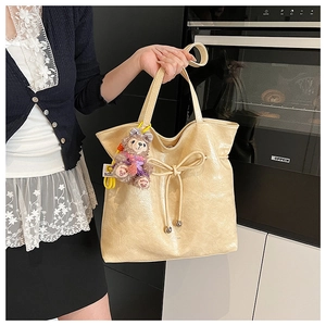 Détail du sac cabas minimaliste en cuir verni beige avec nœud coulissant et breloque en peluche