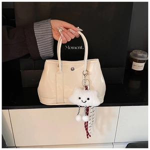 Detail of off-white leather tote with silver clasp and plush cloud charm on a strap