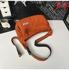 Detail of bright orange nylon crossbody bag with flap pocket and adjustable black strap