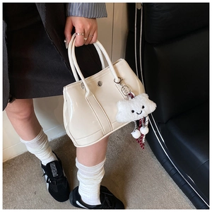Detail of cream patent leather handbag with a plush cloud charm and silver buckle
