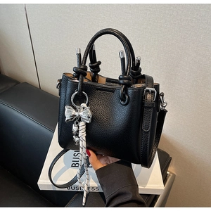 Detail of black pebbled leather bucket bag with silver bow charm and woven rope accent