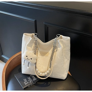 Detail of white snakeskin tote bag featuring pearl chain strap and plush cloud charm