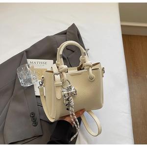 Detail of cream bucket bag with lychee texture, knot handle and bow charm accent