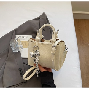 Close-up of cream lychee leather bucket bag with knot handles and bow charm