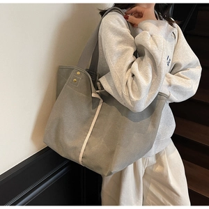Close-up of canvas tote bag with contrast stripe, gold rivets, and thick shoulder straps
