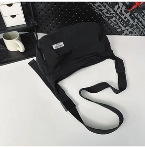 Detail of waterproof black nylon messenger bag with white woven label on white table