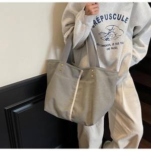 Detail of grey canvas tote bag featuring creamy ribbon and golden metal rivets