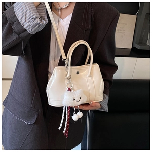Detail of creamy white patent leather handbag with a plush cloud charm and slim strap