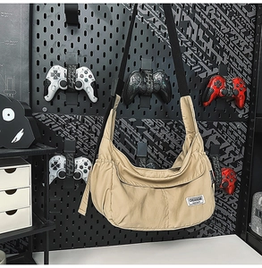 Detail of khaki messenger bag with logo patch on a tech-inspired pegboard background