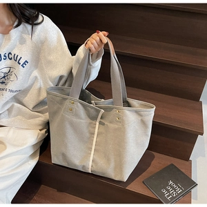 Detail of grey canvas tote bag with leather-wrapped handles on wooden stairs