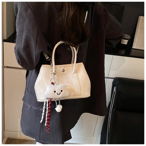 Detail of cream patent leather handbag with glossy finish and plush cloud charm accessory