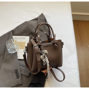 Detail of dark brown lychee leather bucket bag with top handle and woven tassel charm