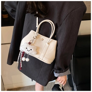 Close-up of white patent leather handbag with fluffy cloud charm on black blazer outfit