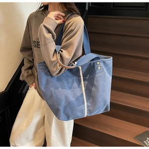 Detail of blue canvas tote bag featuring white contrast stripe and brown leather handles