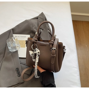 Detailed macro of brown lychee leather bucket bag with woven rope bow and silver hardware