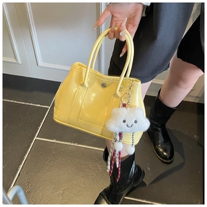 Detail of yellow patent leather handbag with a plush white cloud charm and metal clasp
