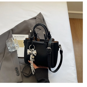 Detail of black lychee grain bucket bag with silver bow charm and twisted rope handle