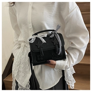 Detail of black square bag featuring star appliques, lace bow, and checkered ribbon handle