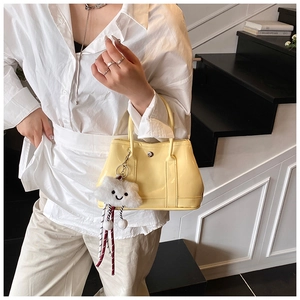 Yellow glossy leather tote bag with a white plush cloud charm held by a model