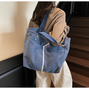 Detail of blue canvas tote bag with white contrast stitching and reinforced metal rivets