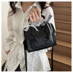 Detail of black vintage satchel with star appliques and lace bow on wooden stairs