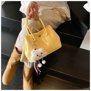 Detail of a bright yellow glossy handbag with a white cloud charm on a double handle
