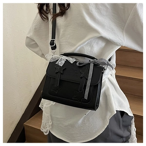 Close-up of black PU messenger bag with star patches and lace bows on wooden stairs