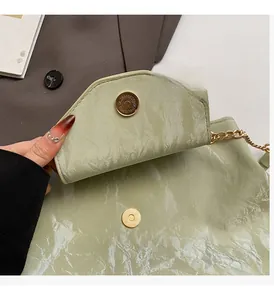 Close-up of golden magnetic clasp and metallic green pleated texture on shoulder bag