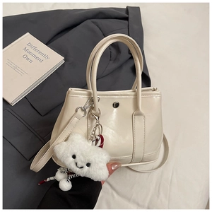 Detail of cream tote bag with silver button and white plush cloud charm on a grey blazer background