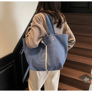 Blue canvas tote bag with off-white trim and gold rivets shown on a shoulder