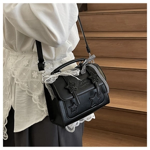 Detail of star-embossed leather messenger bag with white lace and checkered bow on a model